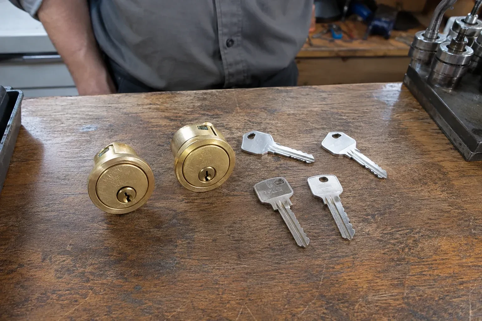 Two detached brass lock cylinders and four house keys on a wooden counter. — Lock Rekeying, Mississauga