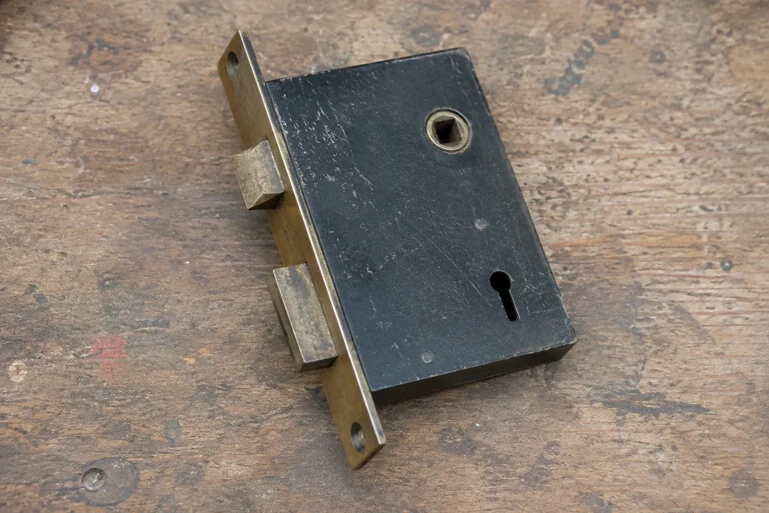 Closed mortise lock case with spindle opening, keyhole, latch and deadbolt on a wooden workbench. — Vintage Mortise Lock Service, Mississauga