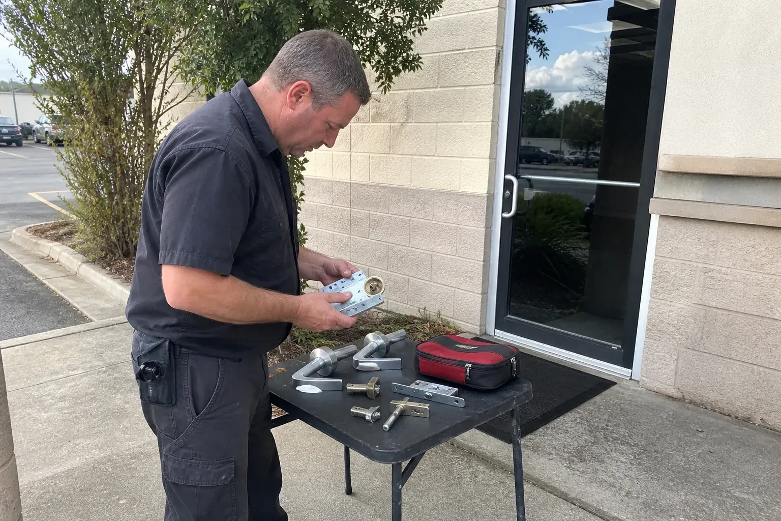 Technician examining detached commercial lock hardware on a table outside a shop entrance. — Business Lockout Service, Mississauga